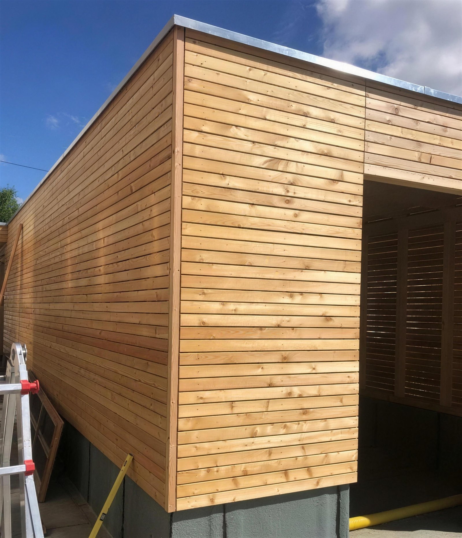 Holzverkleideter Anbau mit offenem Carport und Lamellentor